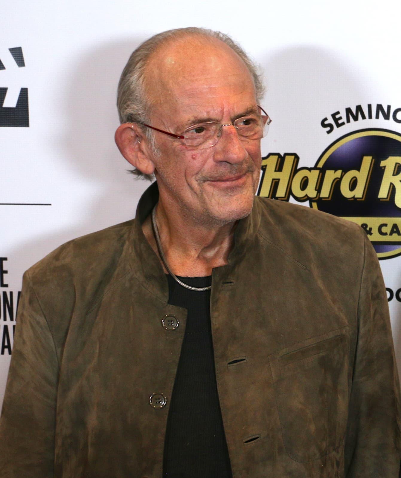 Christopher Lloyd in a brown jacket, smiling on a red carpet
