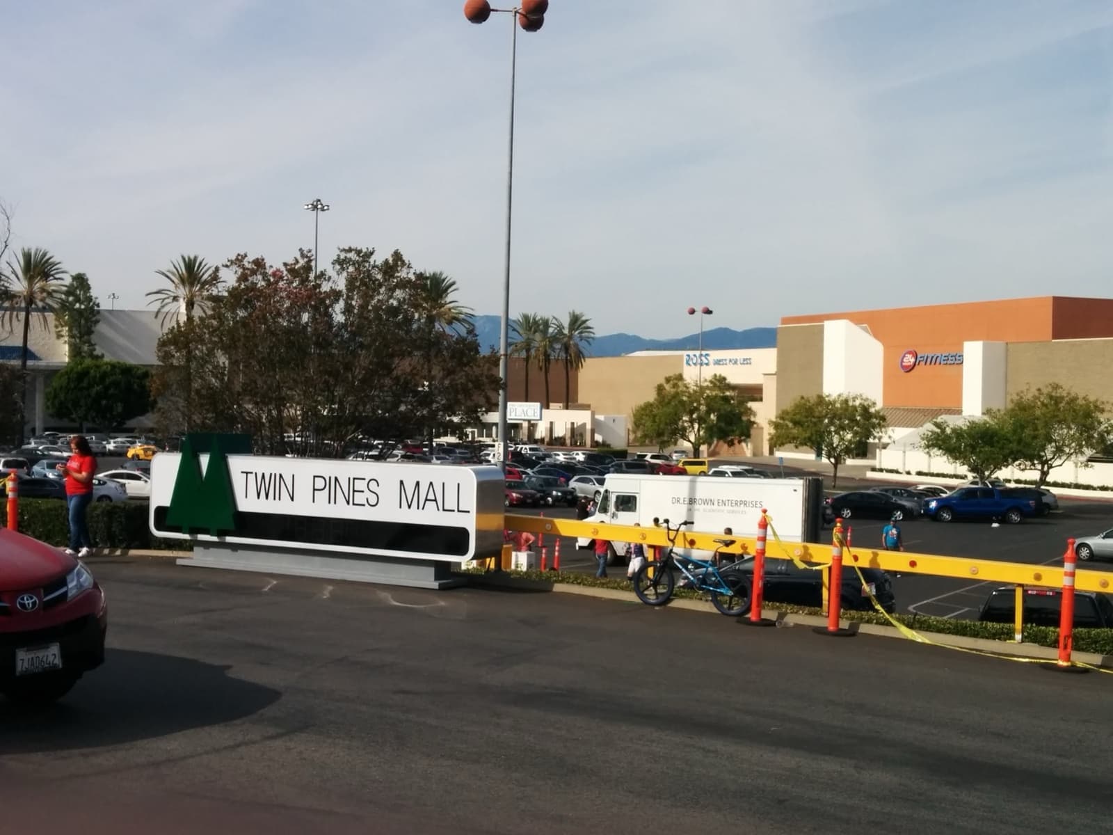A green Twin Pines Mall sign on the edge of a mall car park, with shops behind