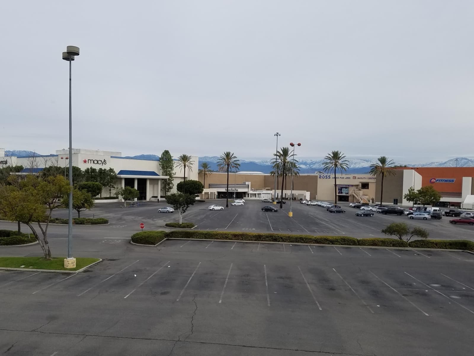 A wide empty car park in front of a mall with a Macy’s store and palm trees