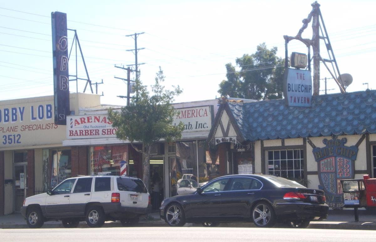 Small shopfronts and parked cars on a sunny boulevard