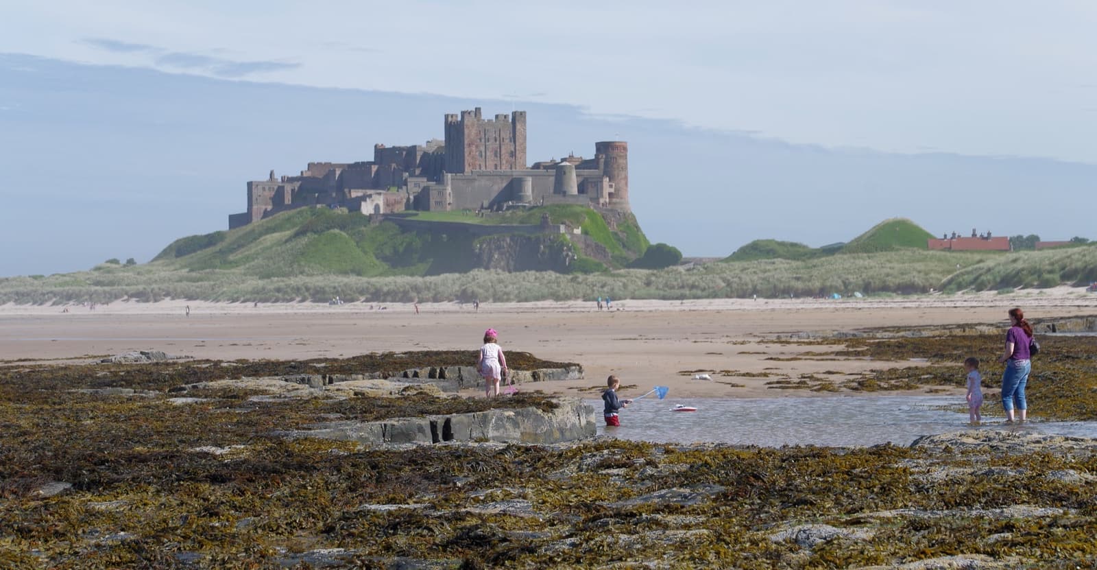 A long stone castle on a rock above a wide sandy beach