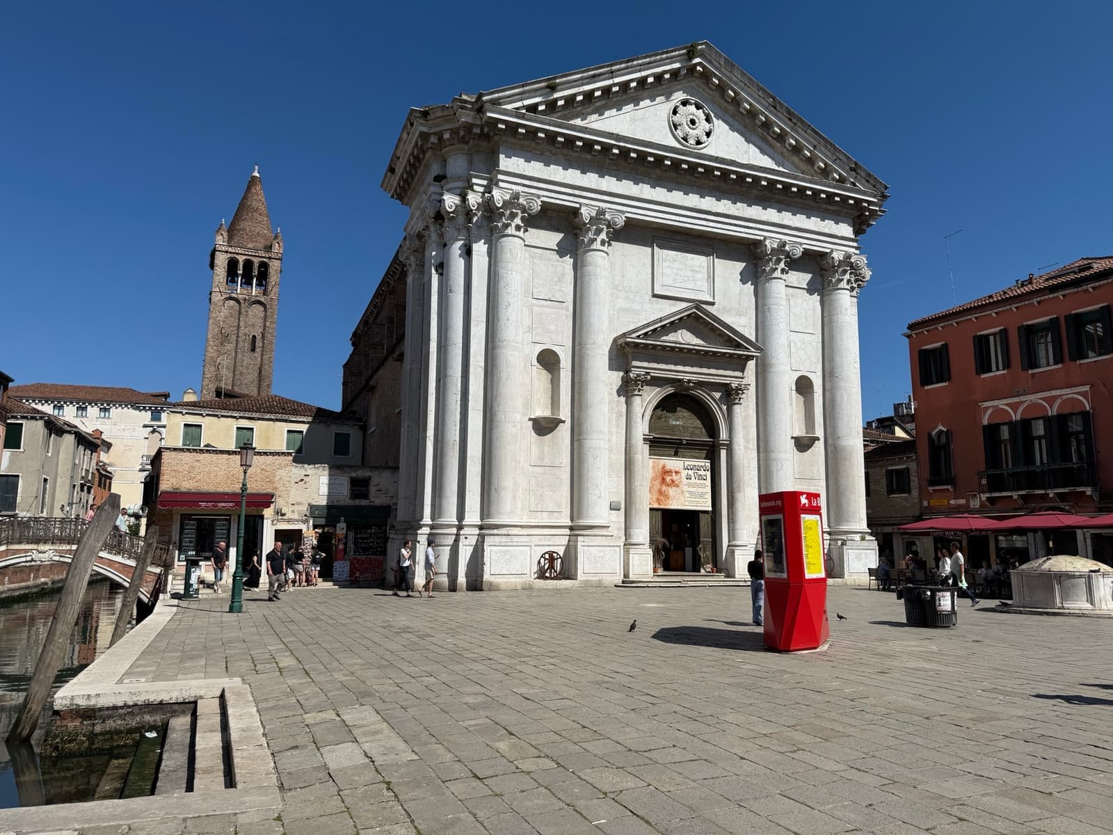 A white classical church front with columns and a triangular pediment on a Venetian square