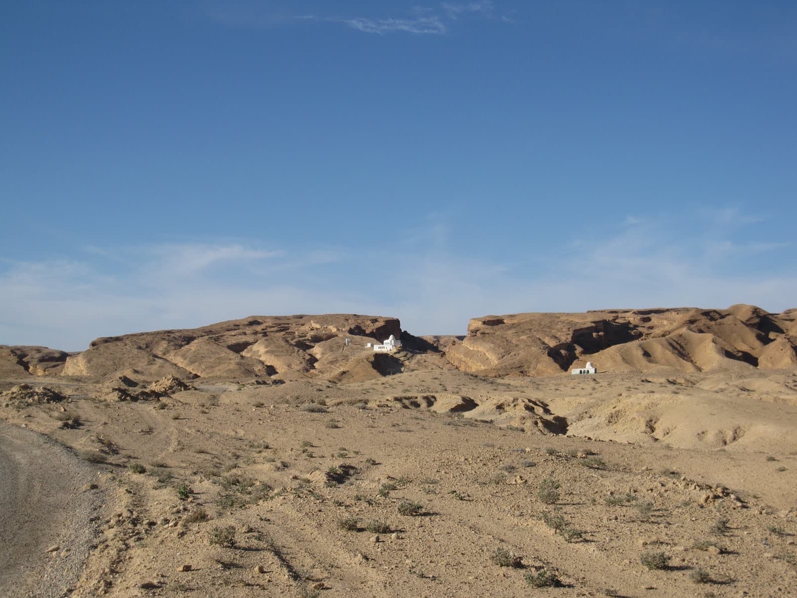 Eroded sandstone ridges and a sandy floor under a blue sky in the Tunisian desert