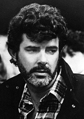 George Lucas with dark curly hair and a beard, in a checked shirt, black and white