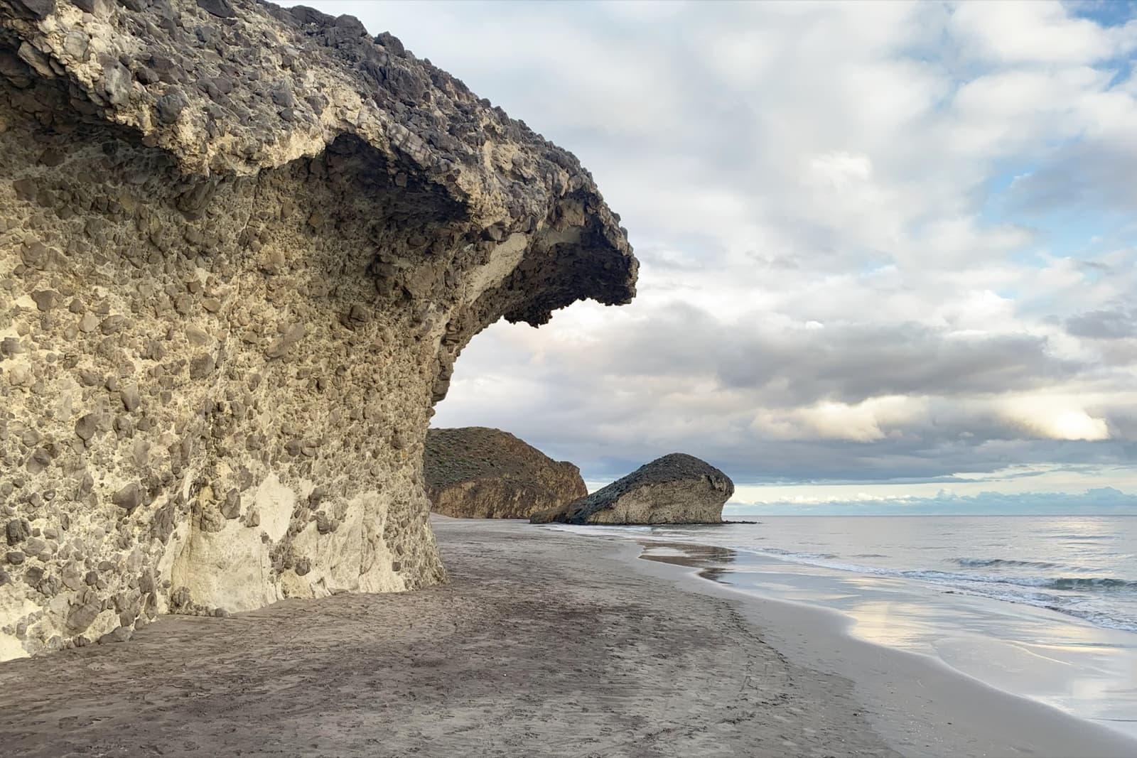 A wave-shaped volcanic rock overhanging the sand on Mónsul beach