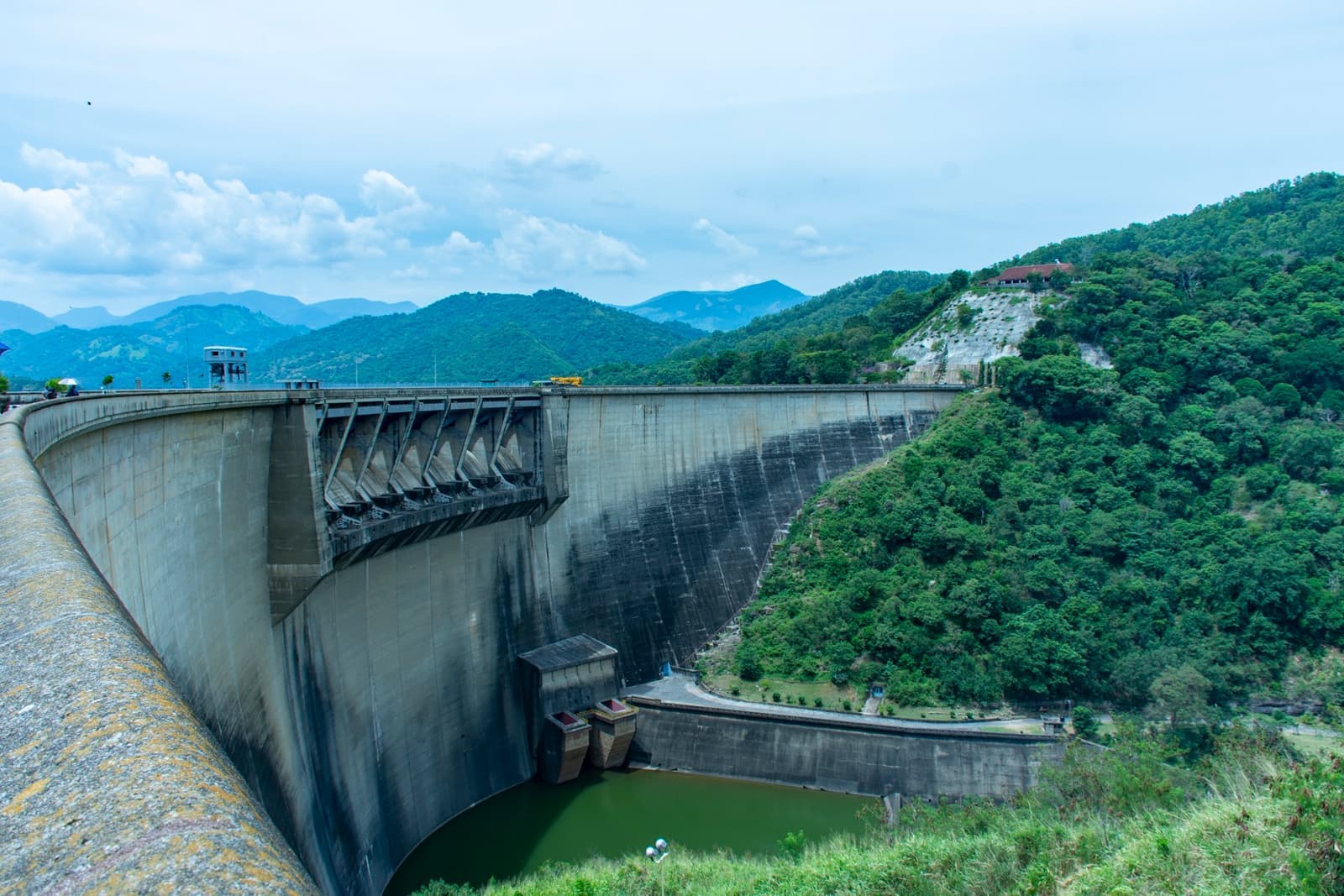 A curved concrete dam wall between green forested hills