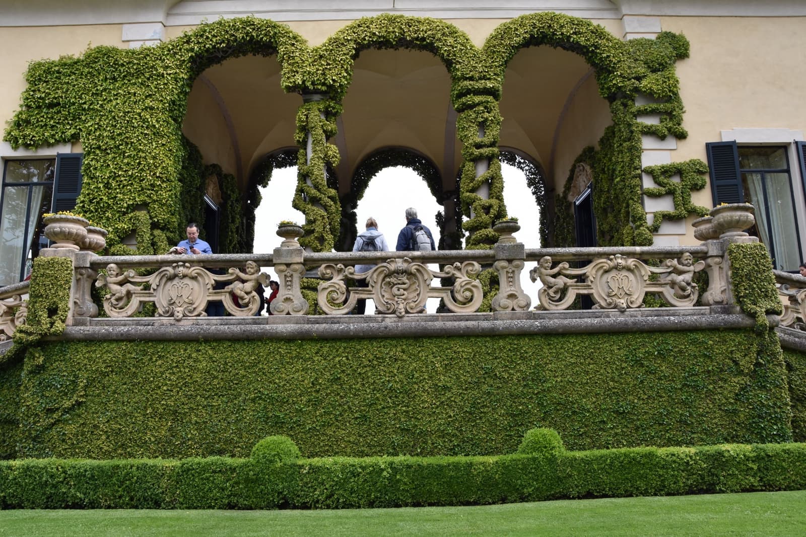 An ivy-covered three-arched loggia above a clipped lawn
