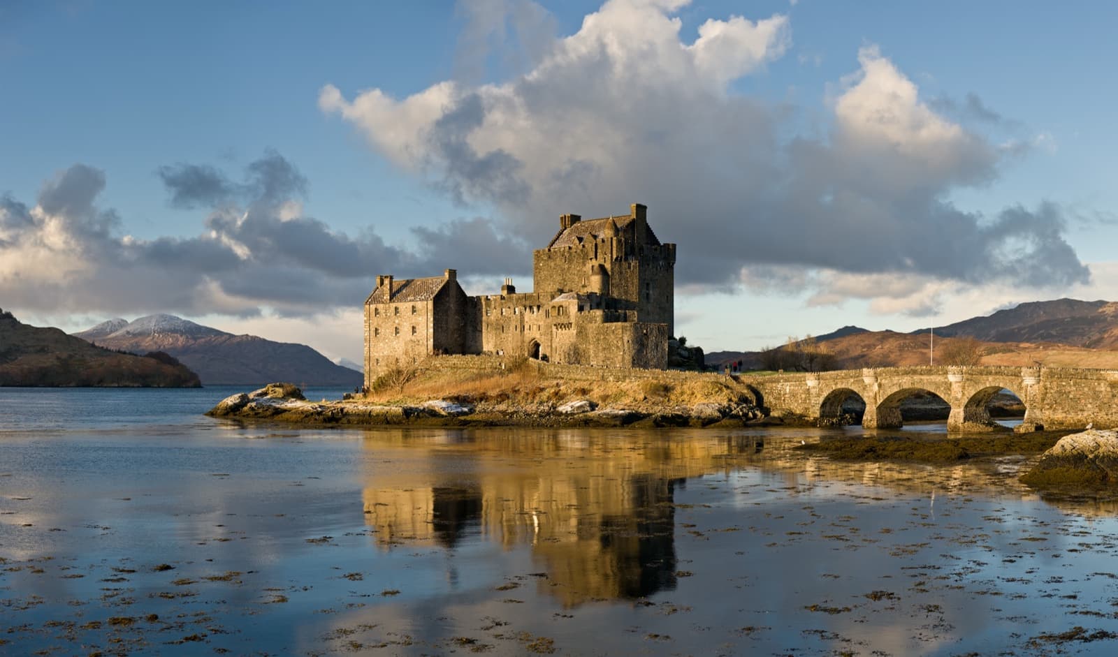 A stone castle on a small island joined to the shore by an arched bridge