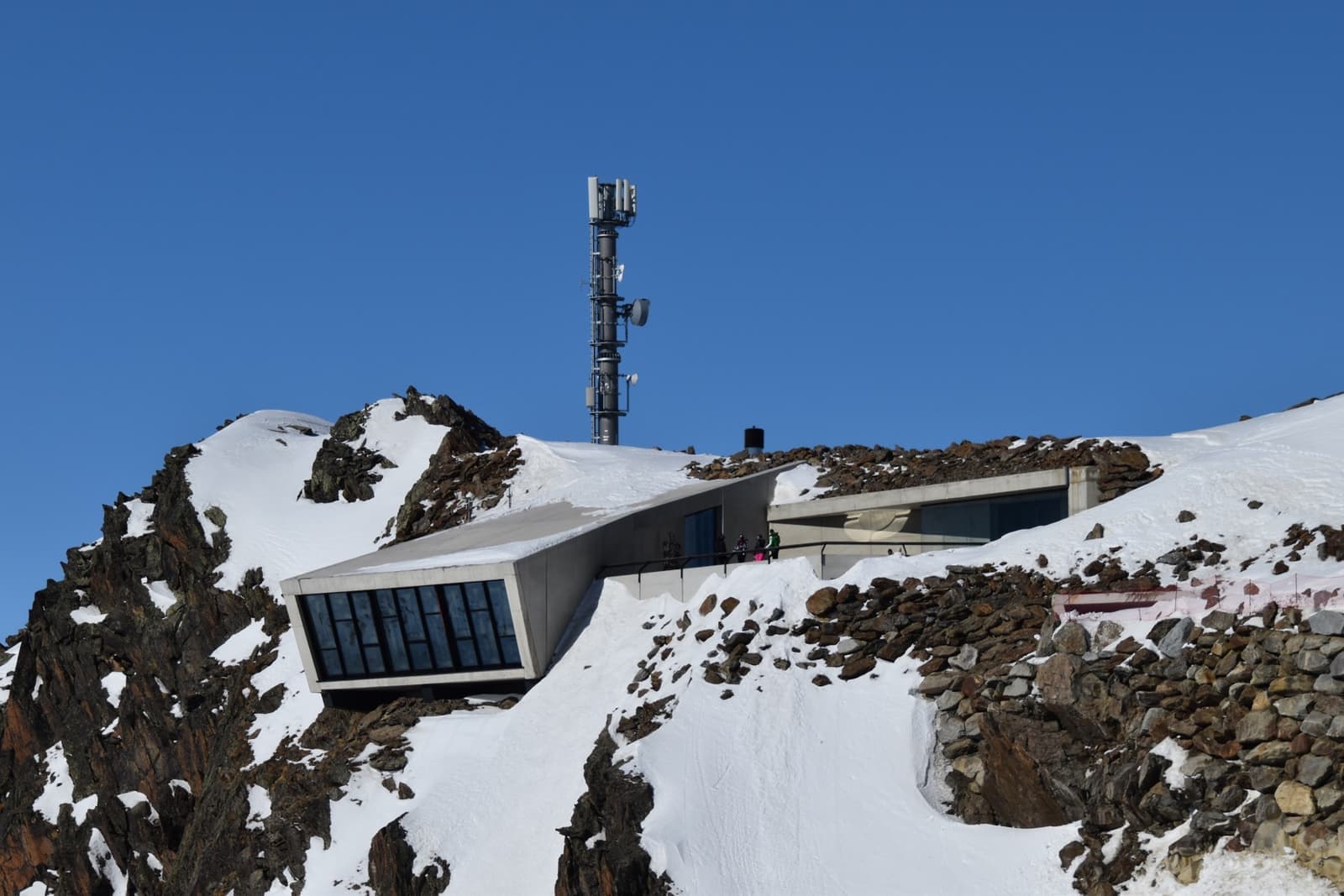 A long concrete building cut into a snowy summit ridge under blue sky