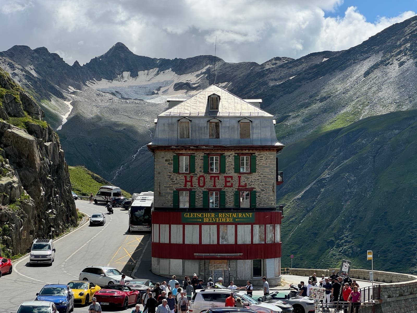 A tall old hotel on a hairpin bend of a mountain road, cars parked outside