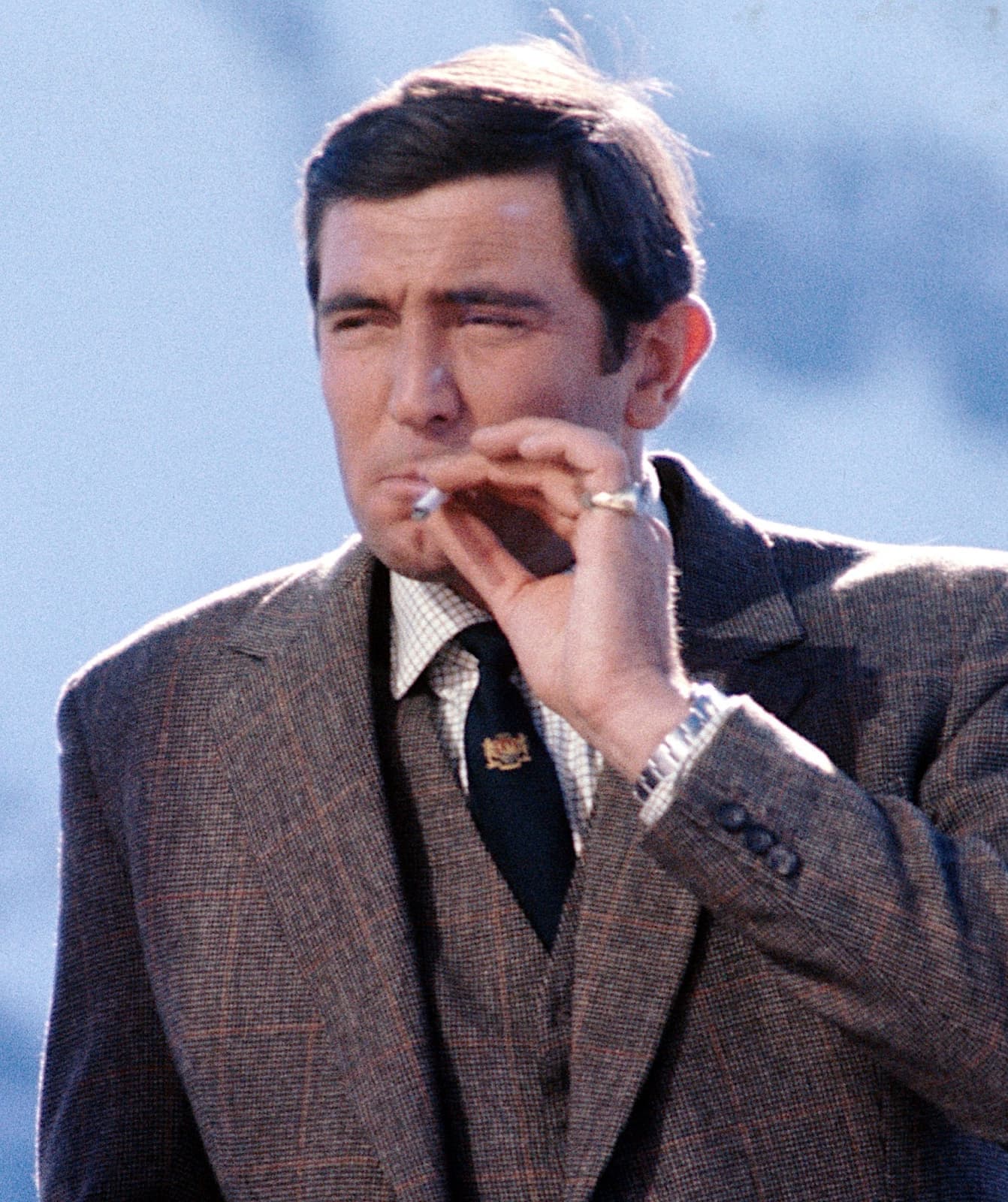 George Lazenby in a tweed suit, lighting a cigarette
