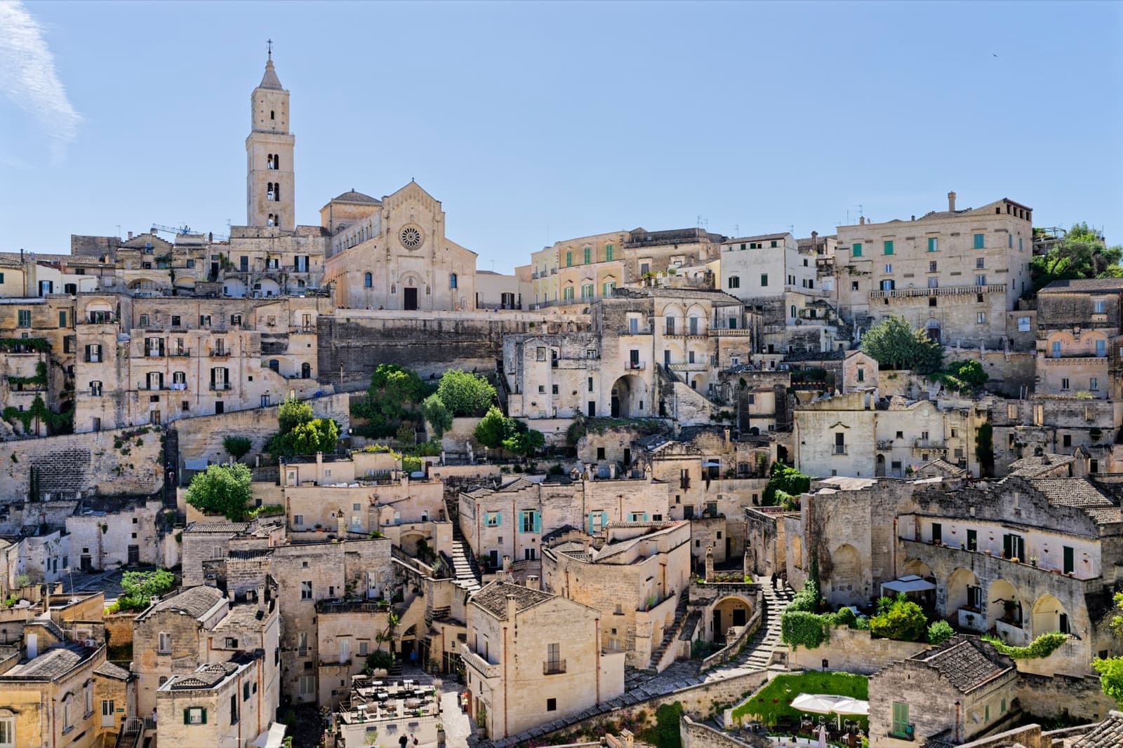 A hillside of pale stone houses and cave dwellings rising to a cathedral bell tower