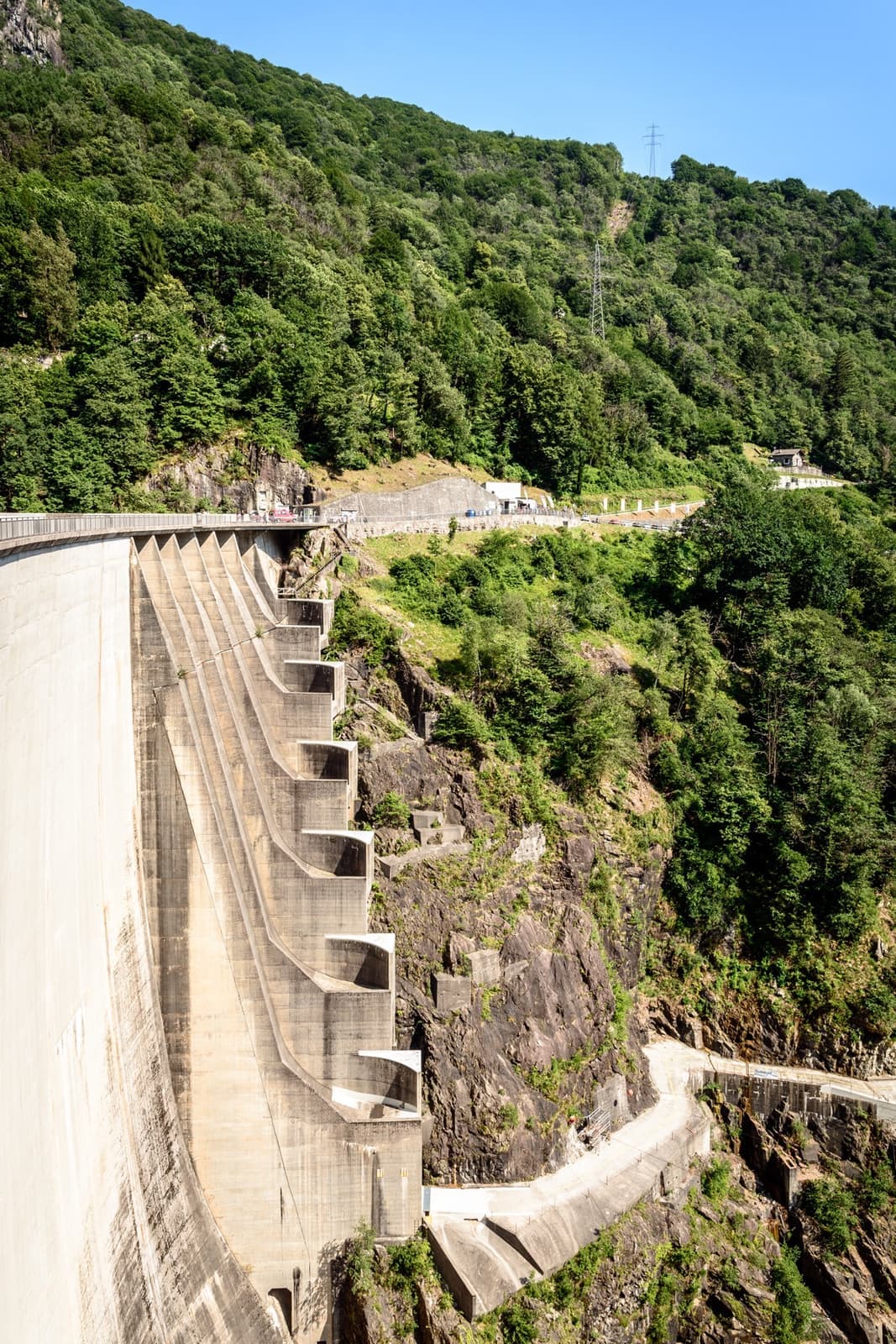 A curved concrete dam wall dropping into a green gorge