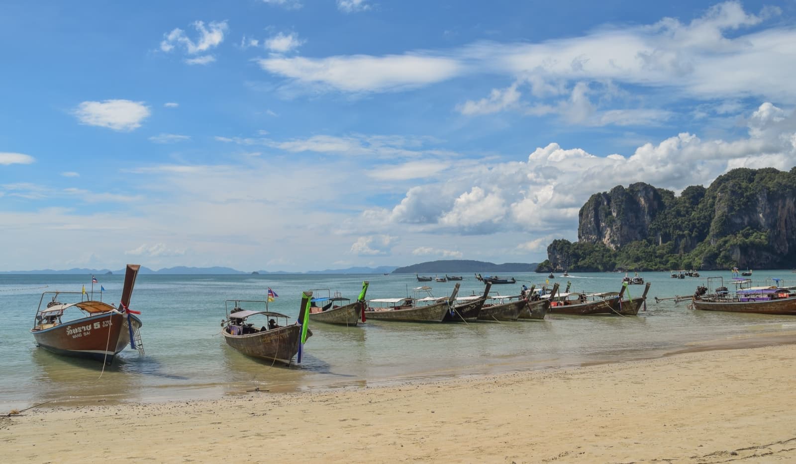 Longtail boats moored on a pale beach below limestone cliffs