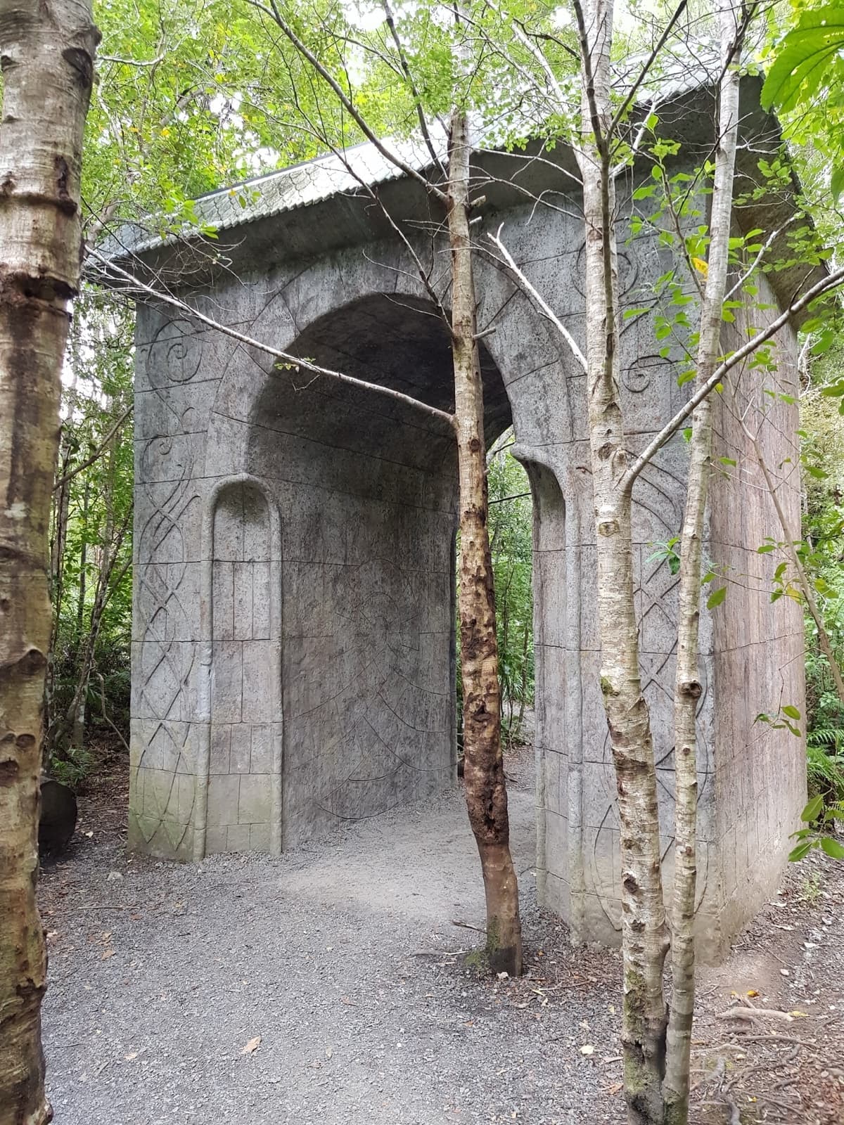 A grey replica archway among young trees on a gravel path