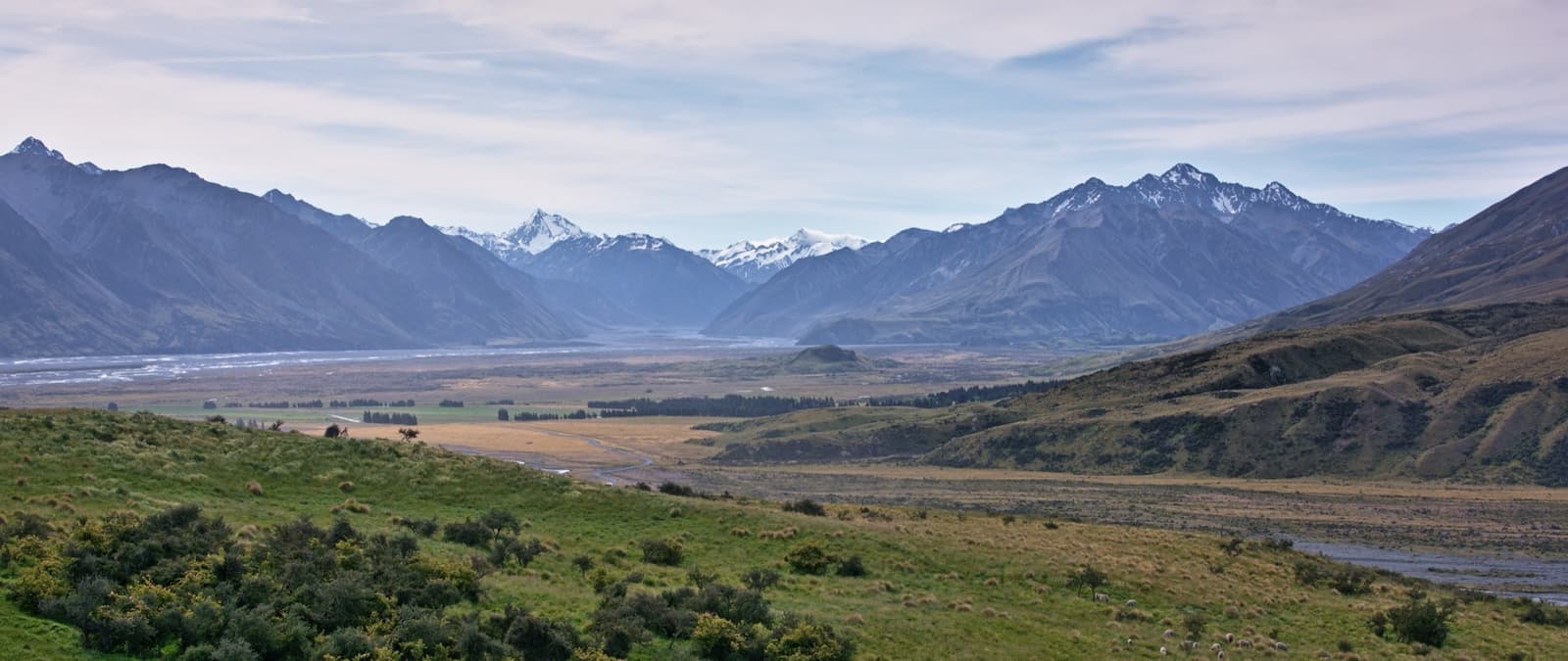 A lone hill rising from a flat braided river valley below mountains