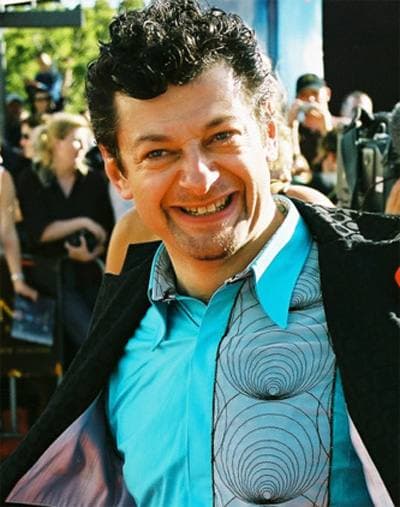 Andy Serkis grins in a turquoise shirt in front of a crowd