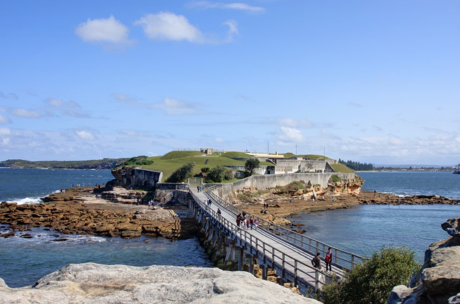 Sandstone fort walls on a small rocky island joined to shore by a wooden bridge