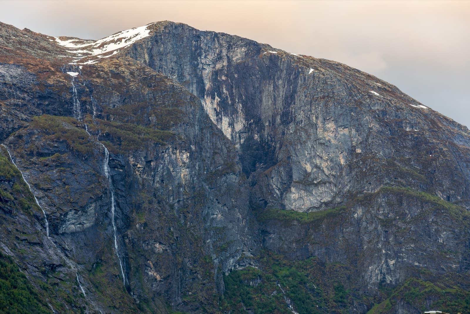 A steep green mountain with a sheer cliff face above a valley