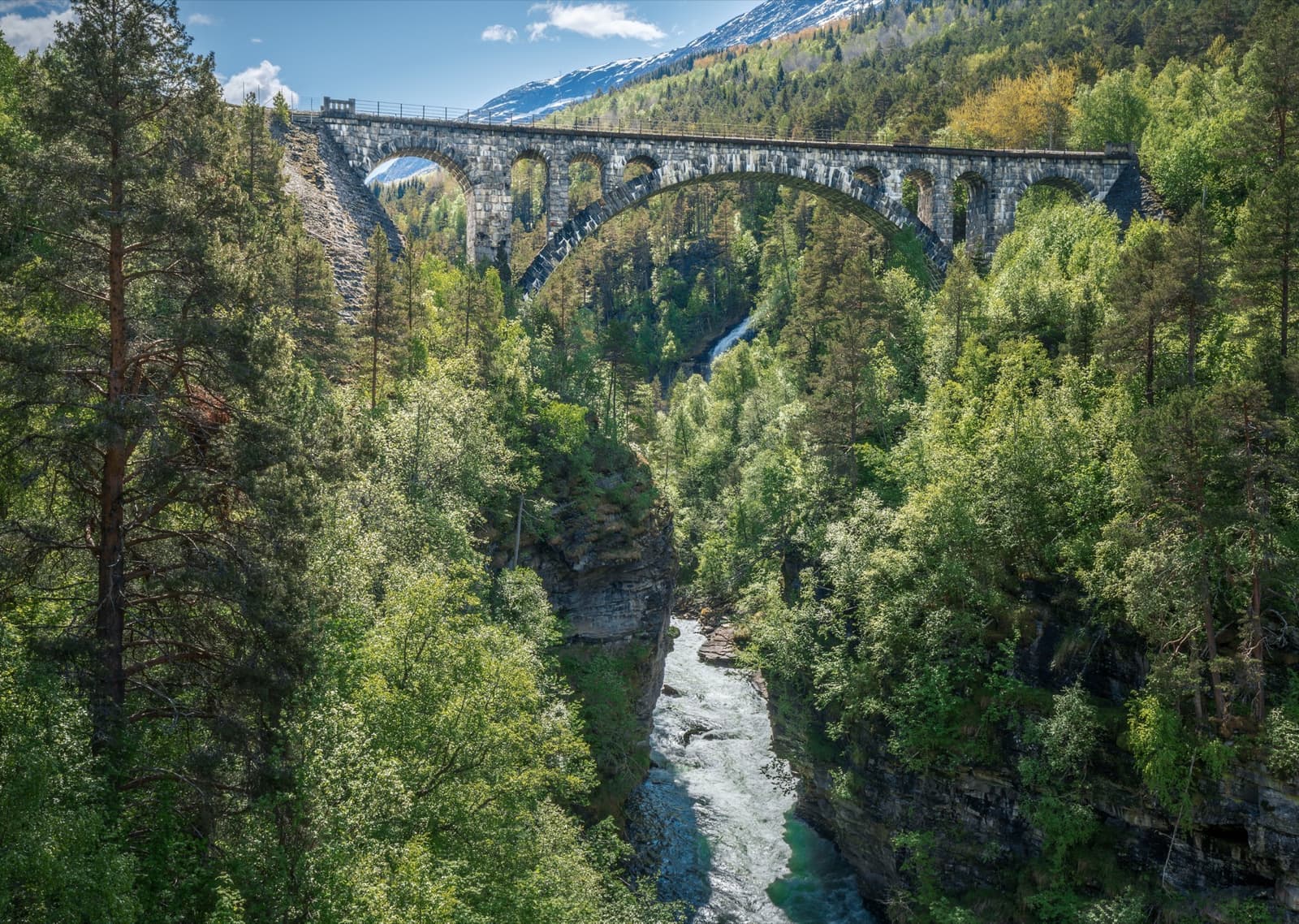A stone railway arch bridge over a green river gorge