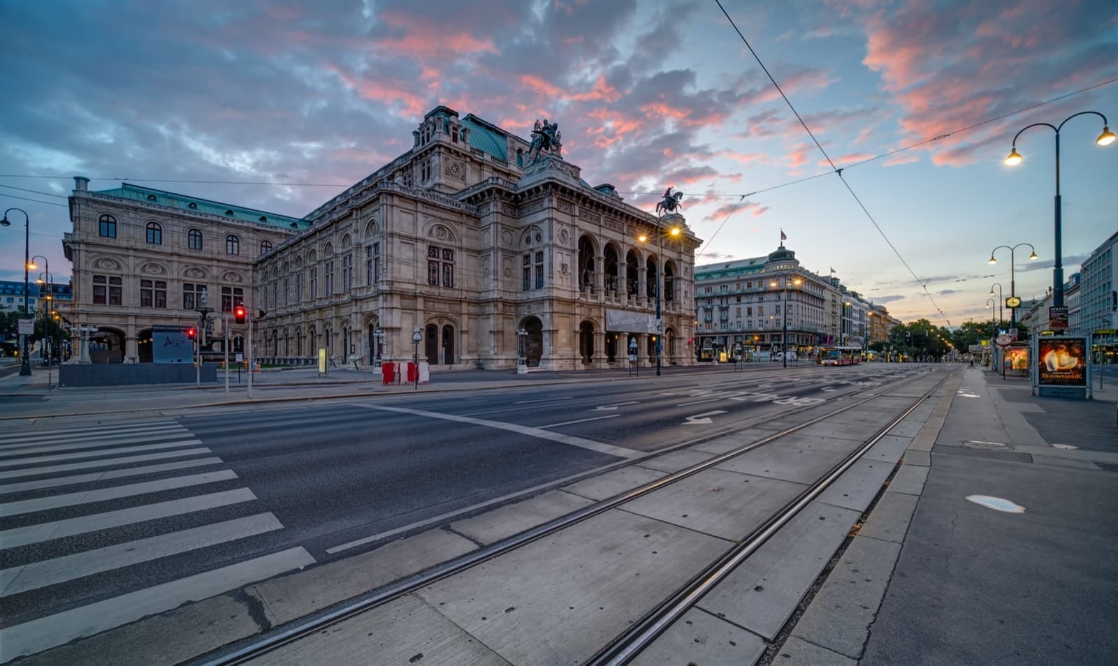 The arcaded stone front of the Vienna State Opera under a pink dawn sky
