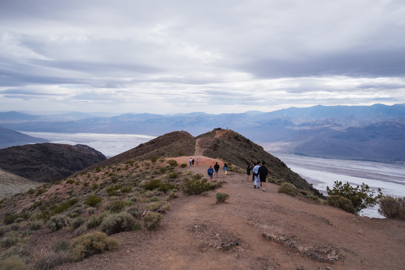 People standing on a ridge above white salt flats and distant mountains