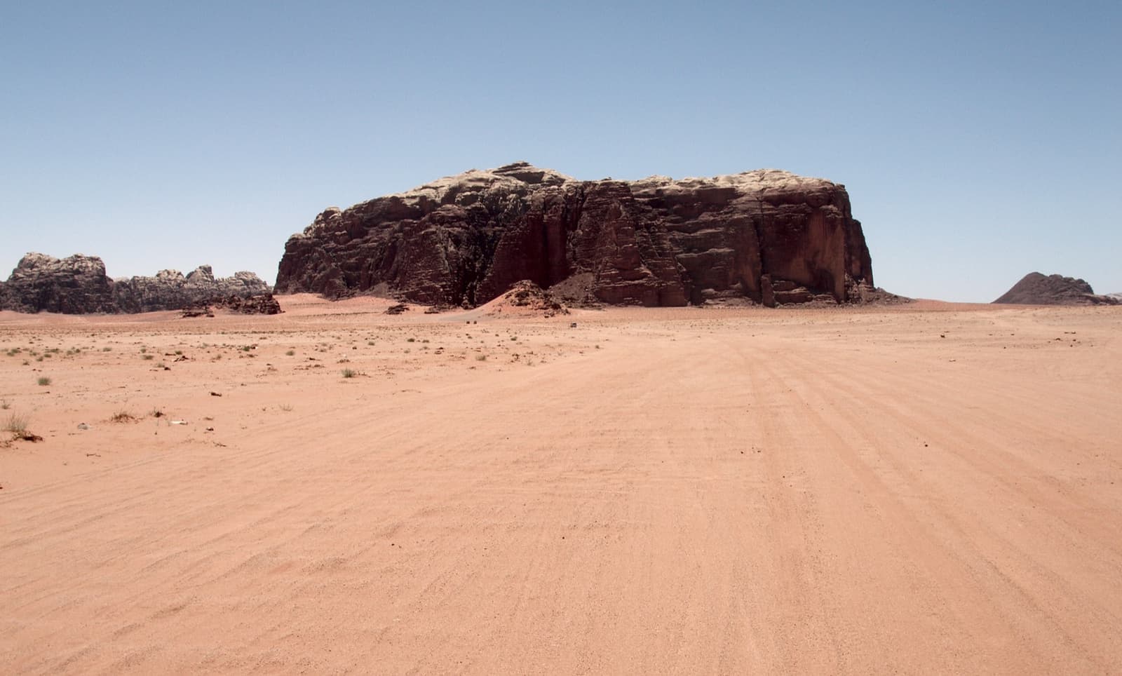 Red sand stretching to sandstone mountains under a blue sky