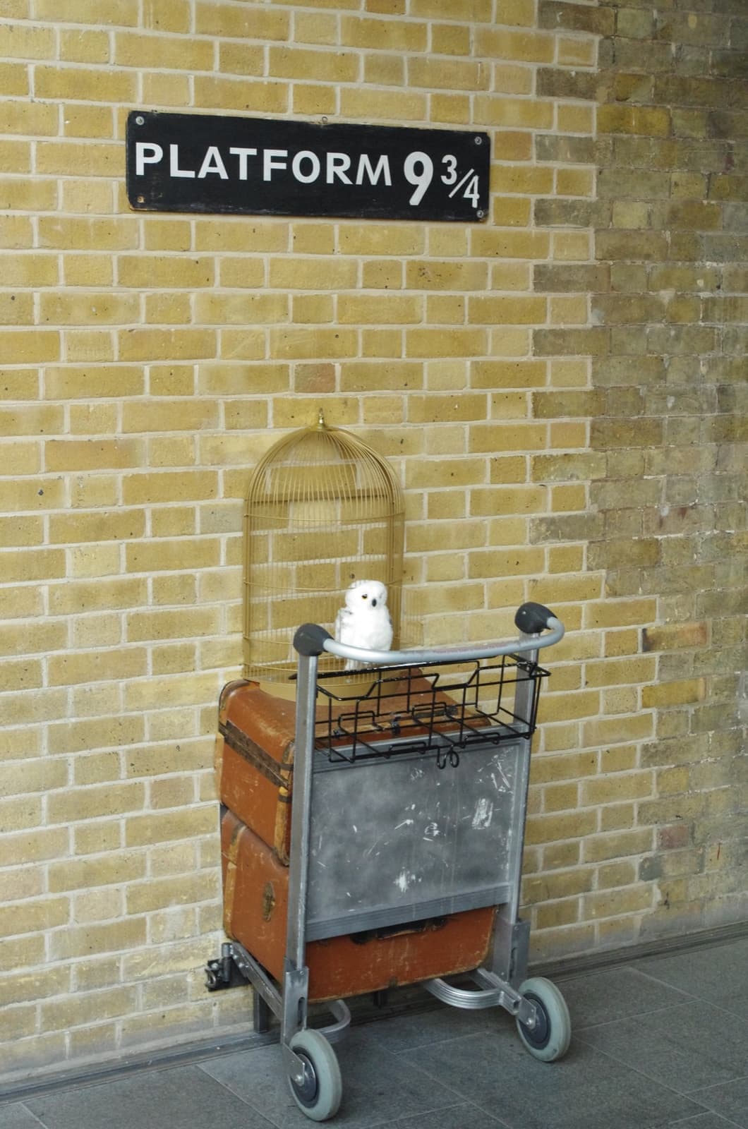 A luggage trolley with a trunk half-sunk into a brick wall under a Platform 9¾ sign