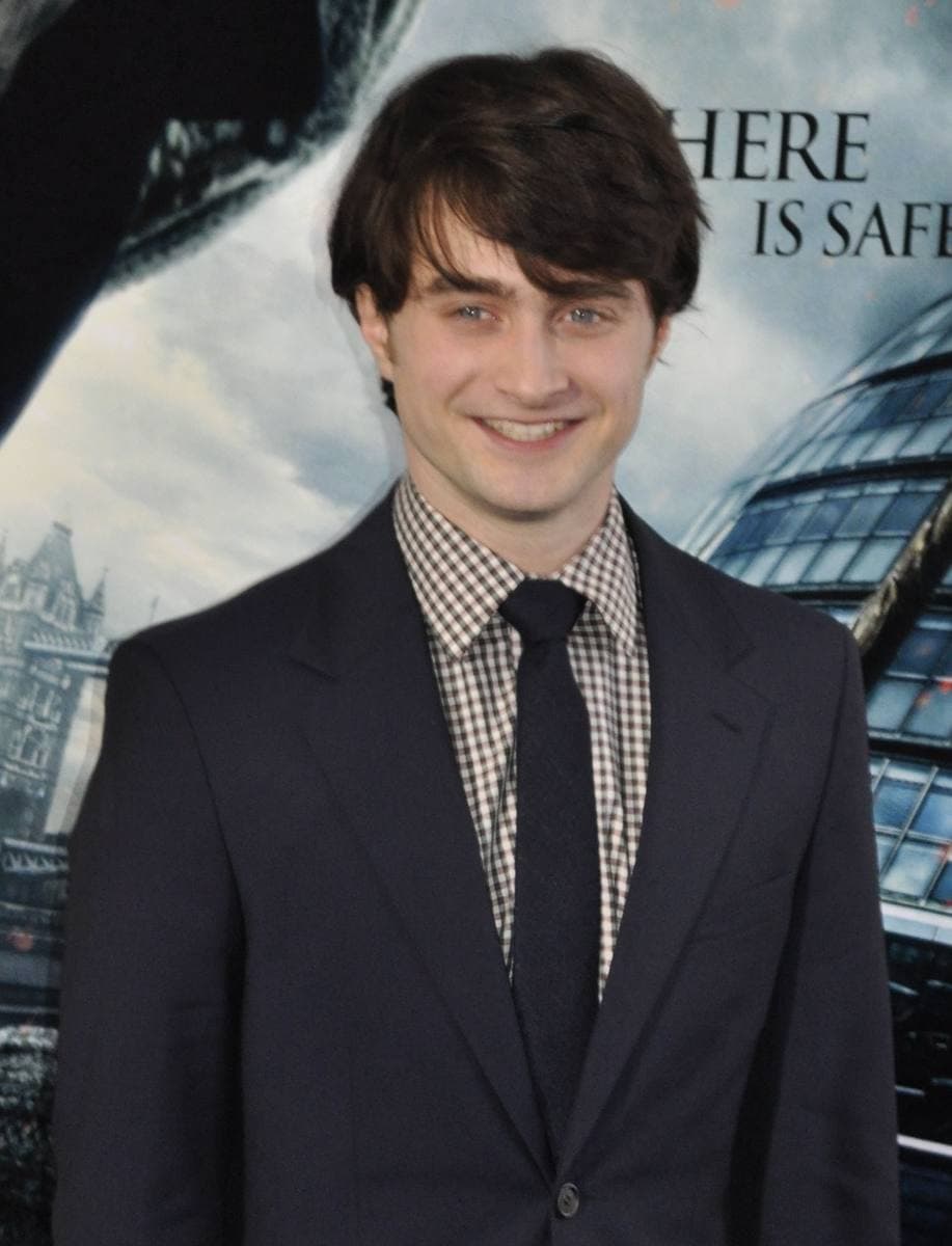 Daniel Radcliffe in a dark suit and checked shirt, smiling