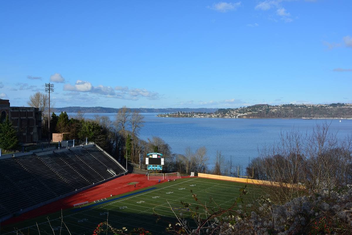 A football field in a gulch below concrete stands, with Commencement Bay beyond