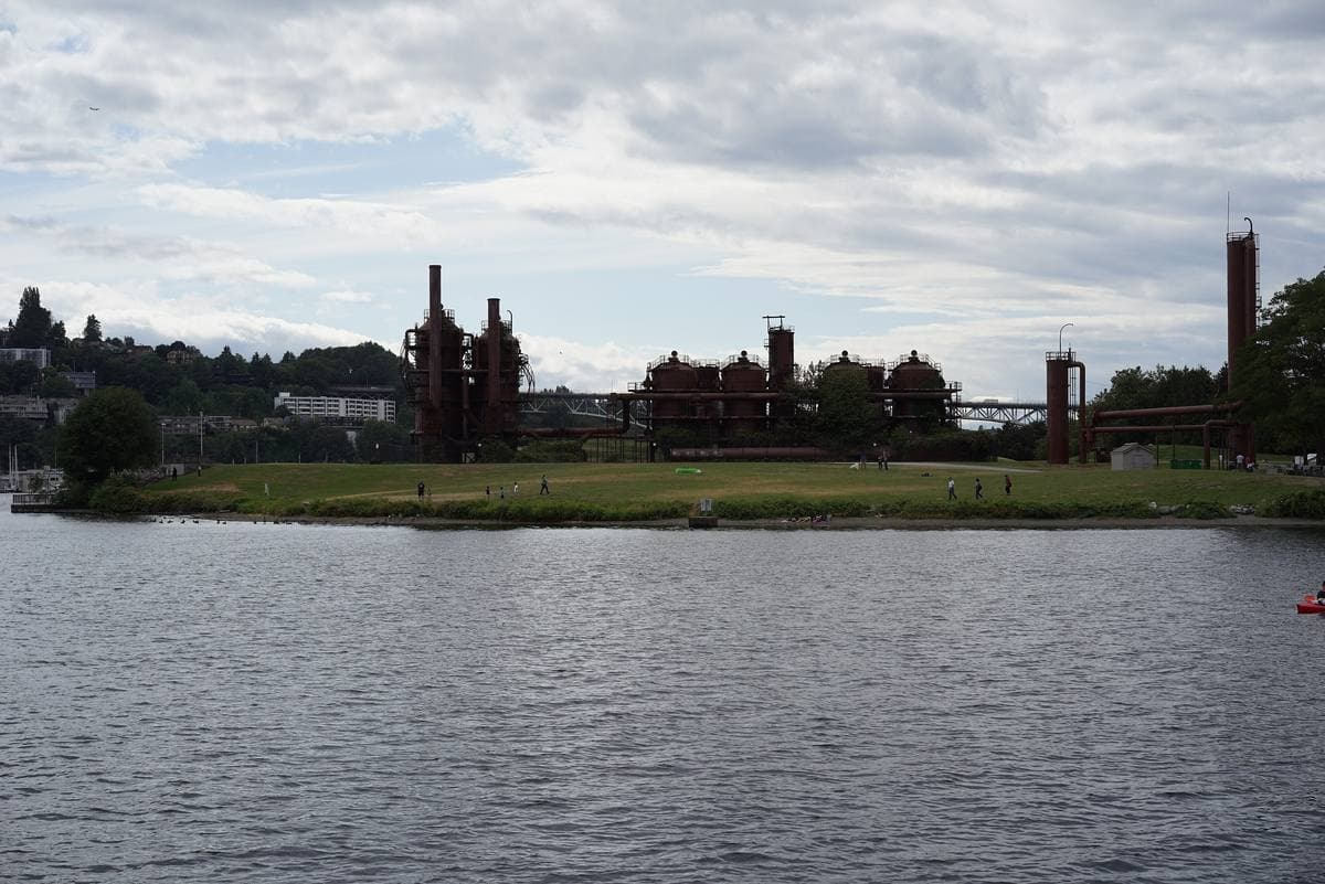 Rusted gas-plant towers on a green shore across the water