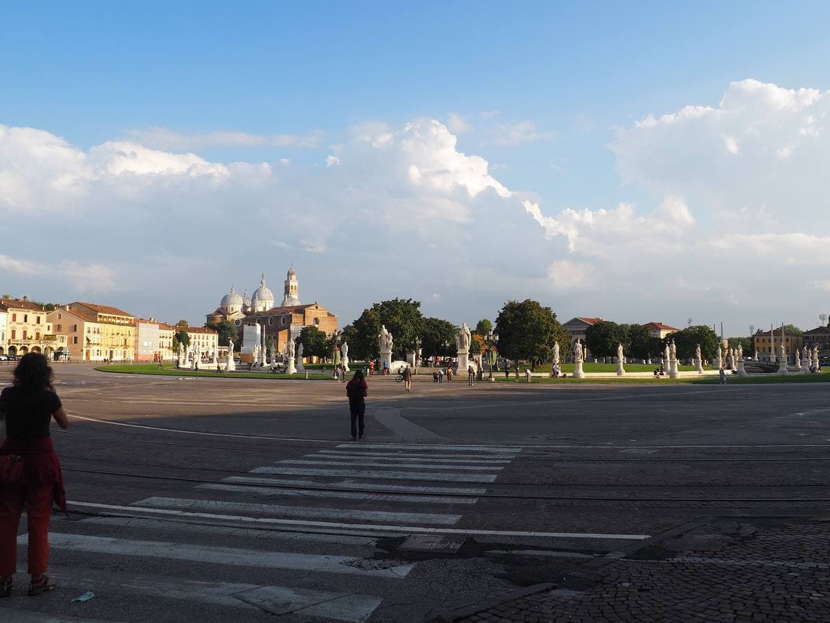 A wide oval piazza in Padua with statues and a domed basilica