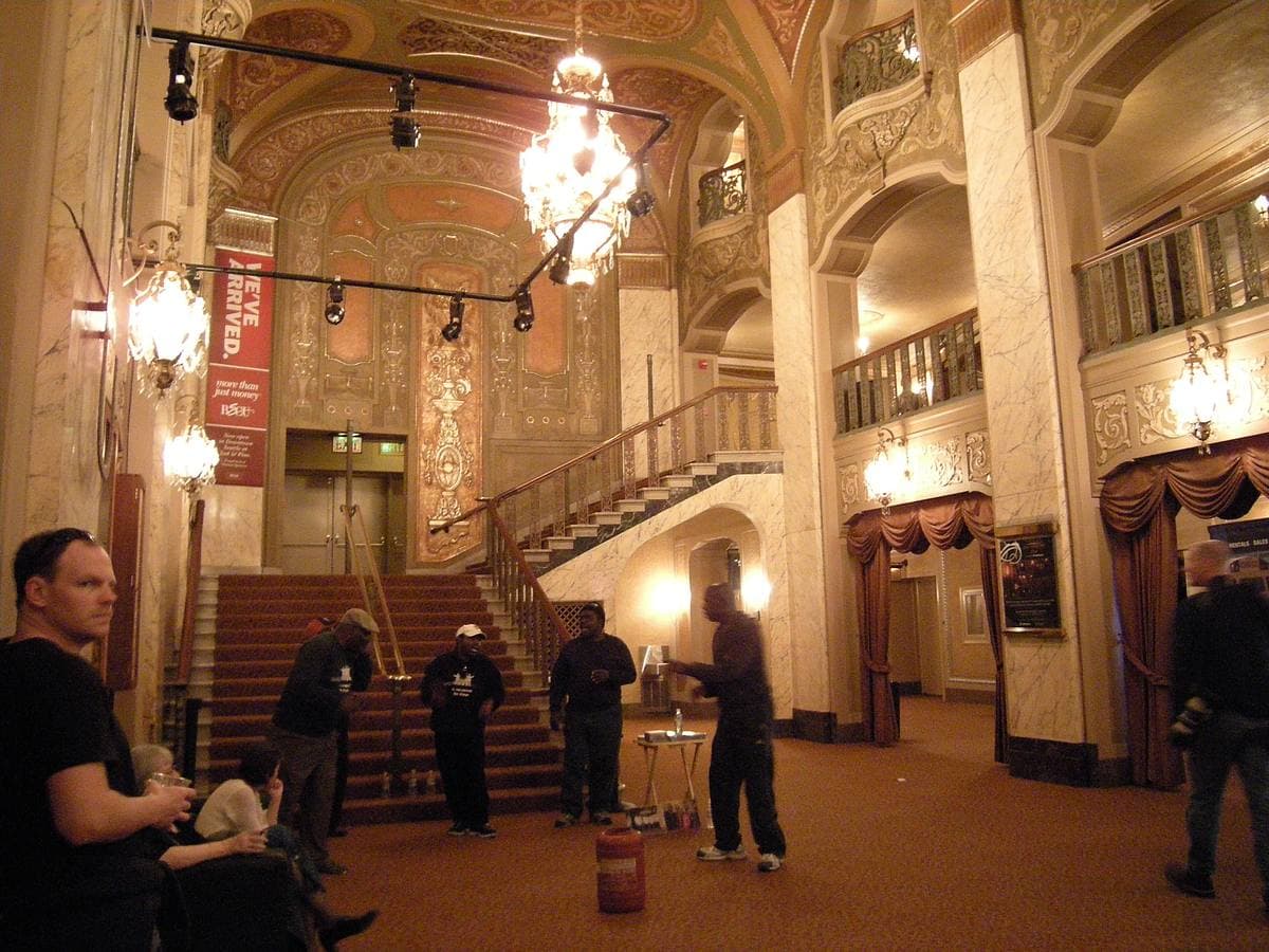 A gilded theatre lobby with chandeliers and a grand staircase