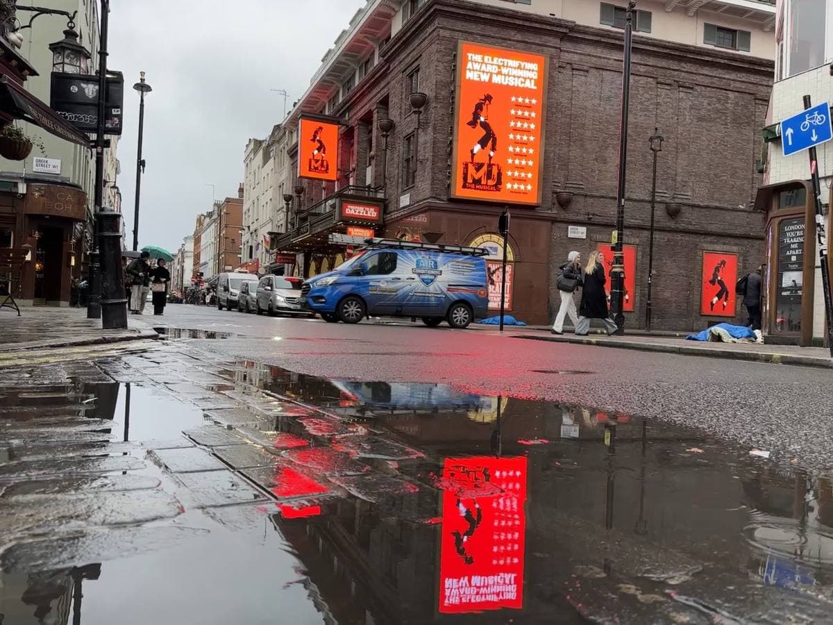 A brick corner theatre with red posters reflected in a wet street