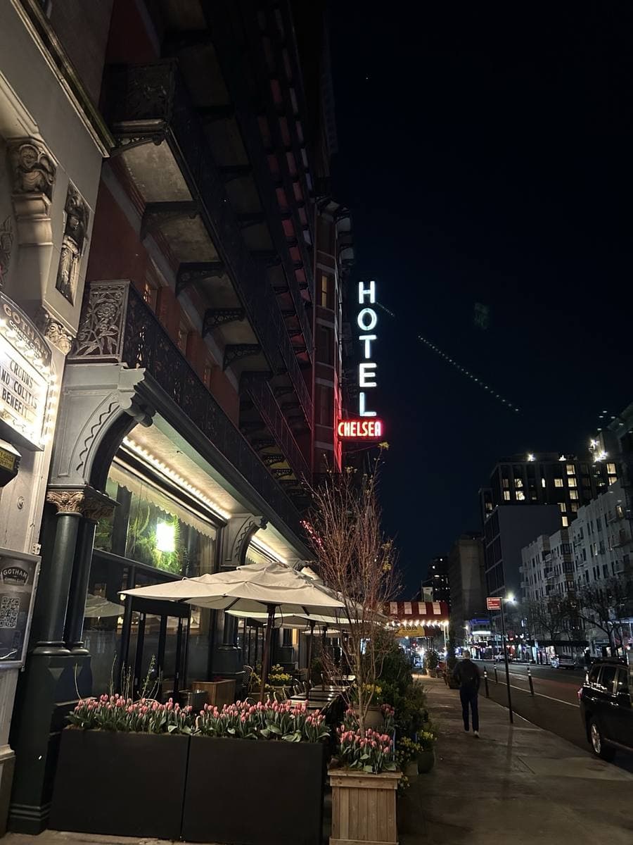 A red-brick hotel at night with a vertical neon HOTEL sign and tulips outside