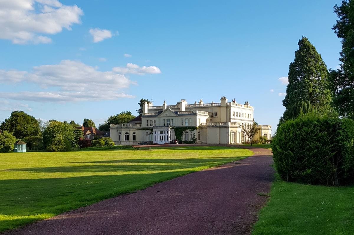 A long cream country house across a lawn, a path running towards it