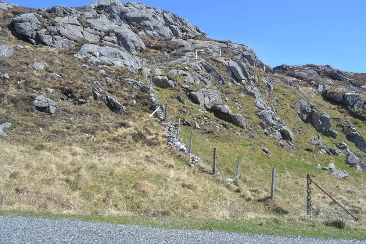 A hillside of grey bare rock and rough grass above a single-track road