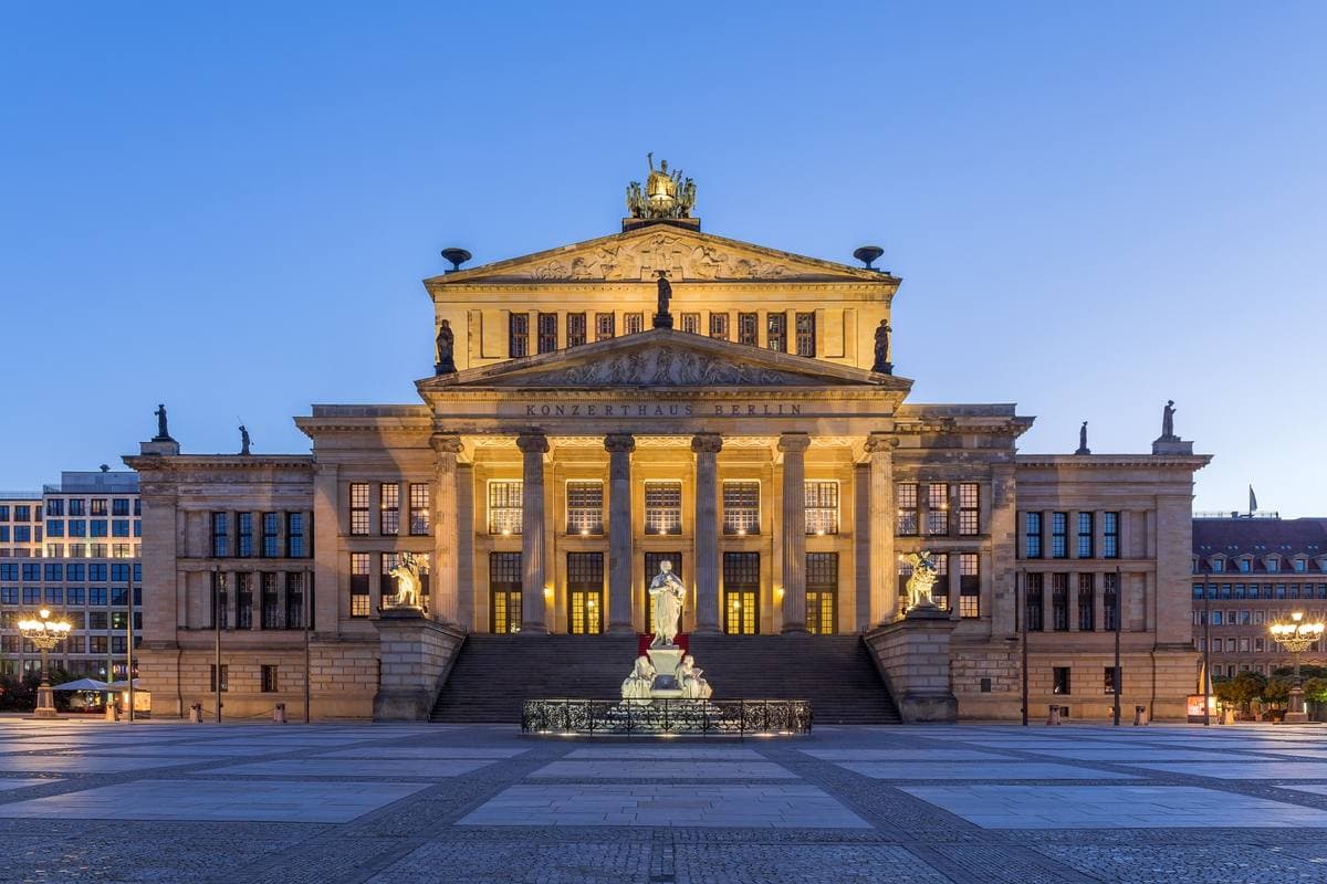 A columned neo-classical concert hall lit gold at dusk over a wide square