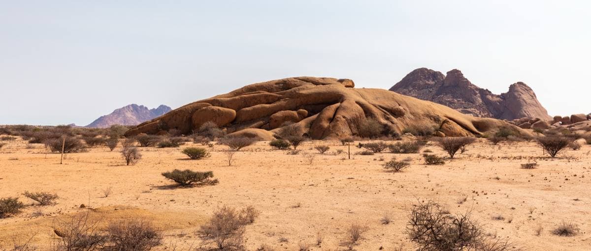 A low granite dome and sharp peaks over a dry plain of scrub and sand