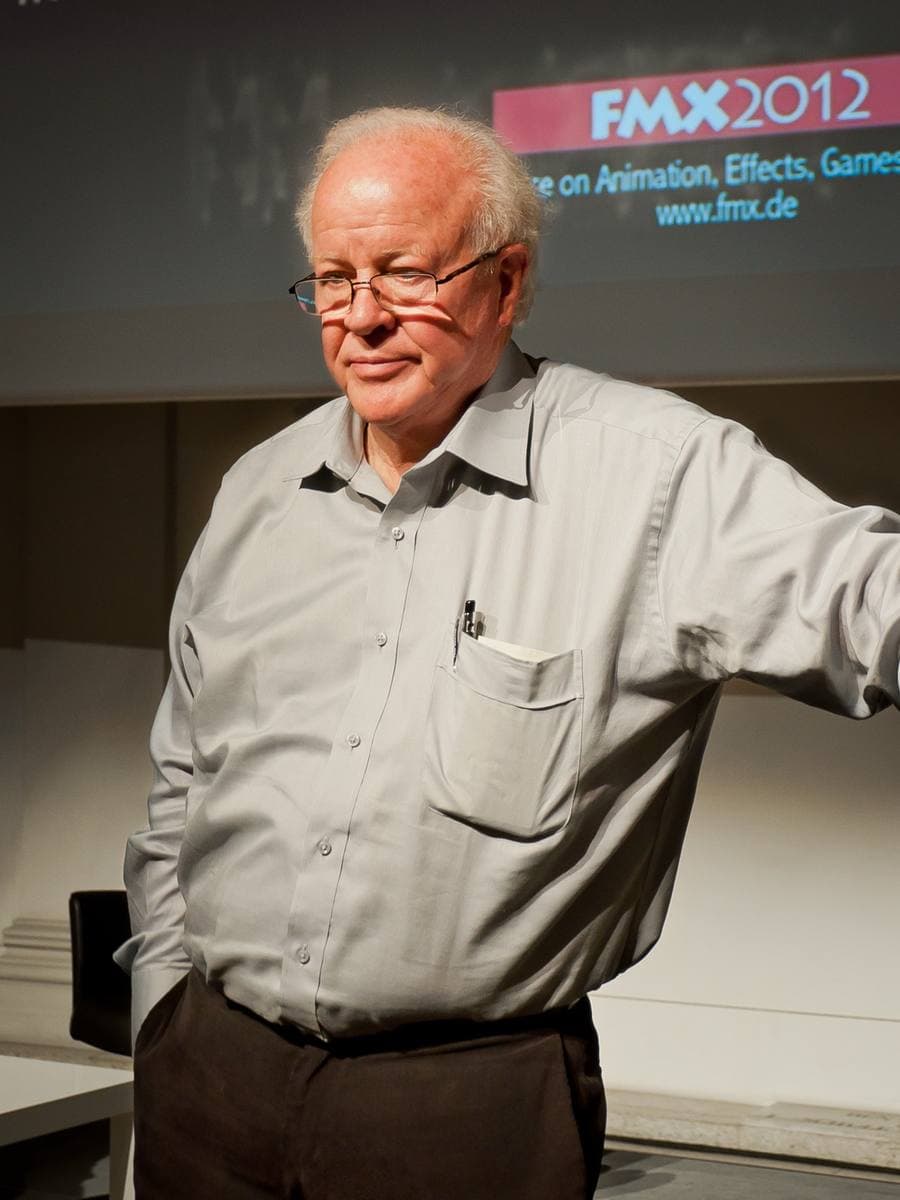 Douglas Trumbull, white-haired, in a grey shirt, gesturing during a talk