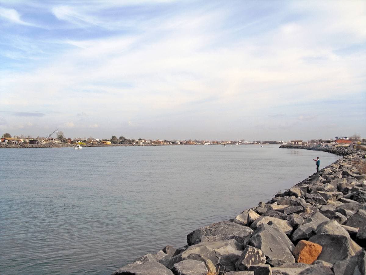 A rock breakwater running along a wide river mouth under a pale sky
