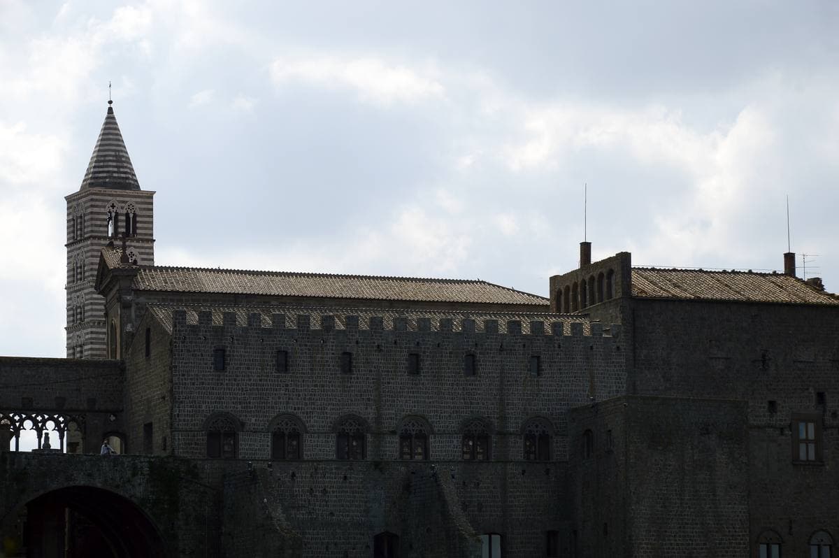 A dark stone medieval palace and bell tower under a pale sky