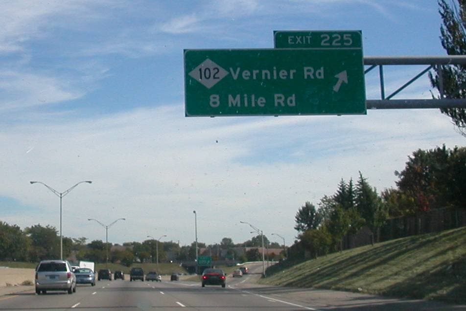 A green motorway sign over a freeway reading 102, Vernier Rd, 8 Mile Rd, Exit 225