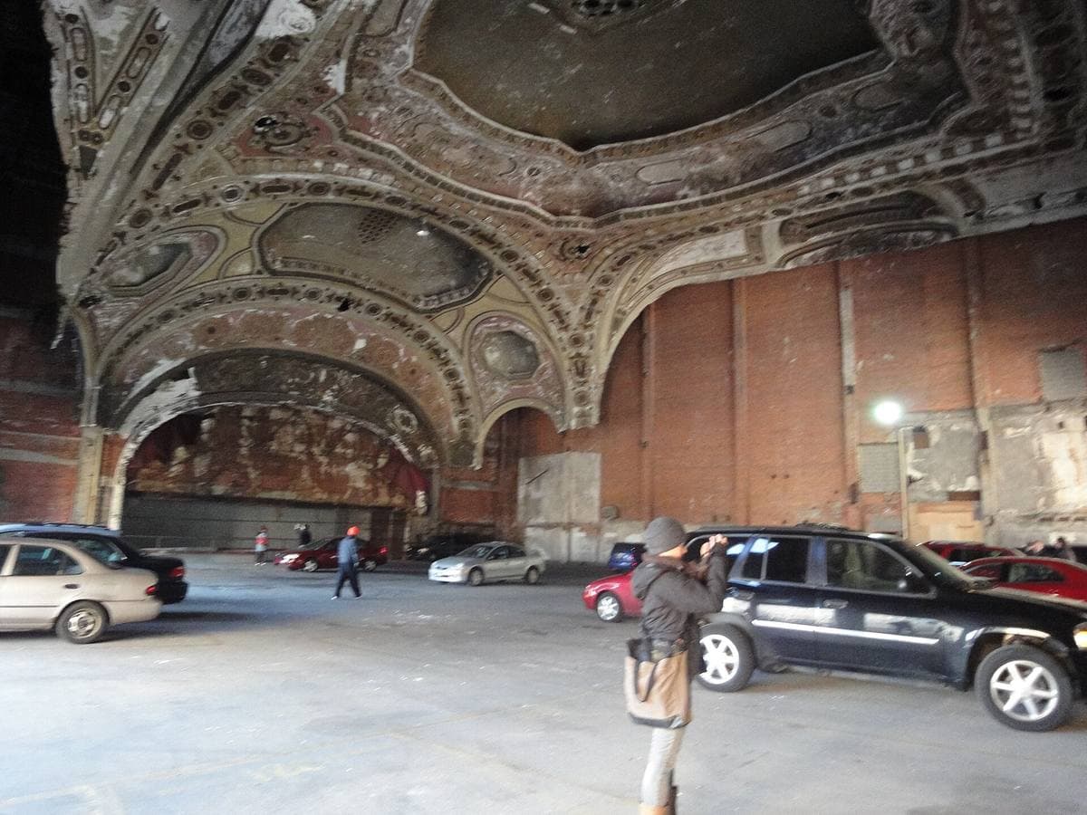 Cars parked on a concrete deck beneath a vast, crumbling ornate theatre ceiling and arch