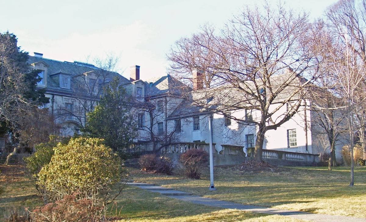 A pale stone mansion behind bare trees and a winter lawn