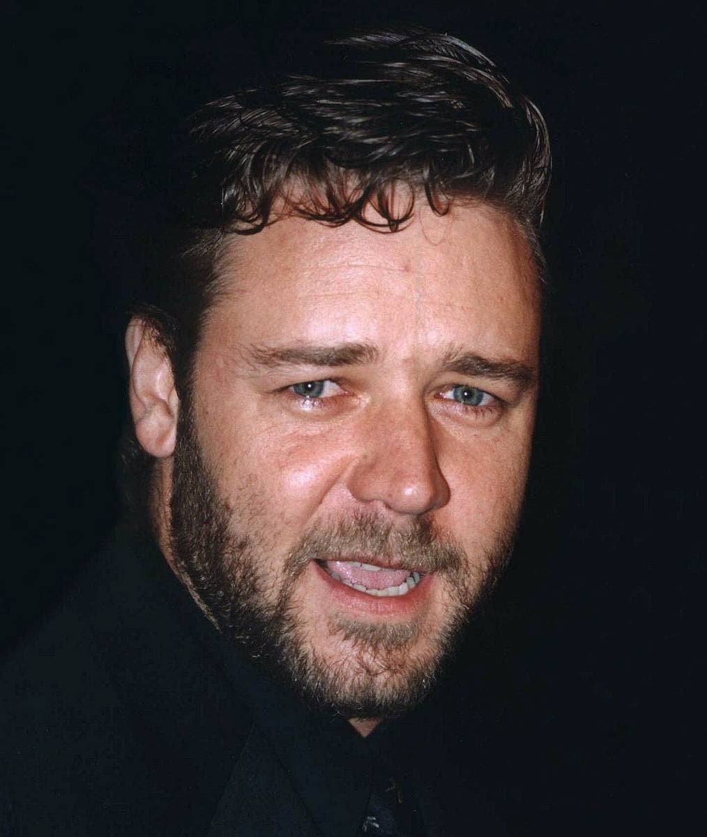 Russell Crowe, bearded with dark curly hair, smiling, in a dark shirt