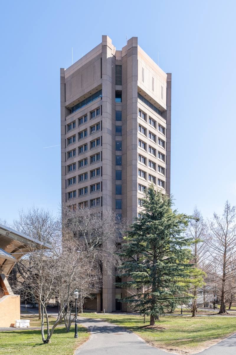 A tall brown-brick tower with ribbon windows above bare trees and a lawn