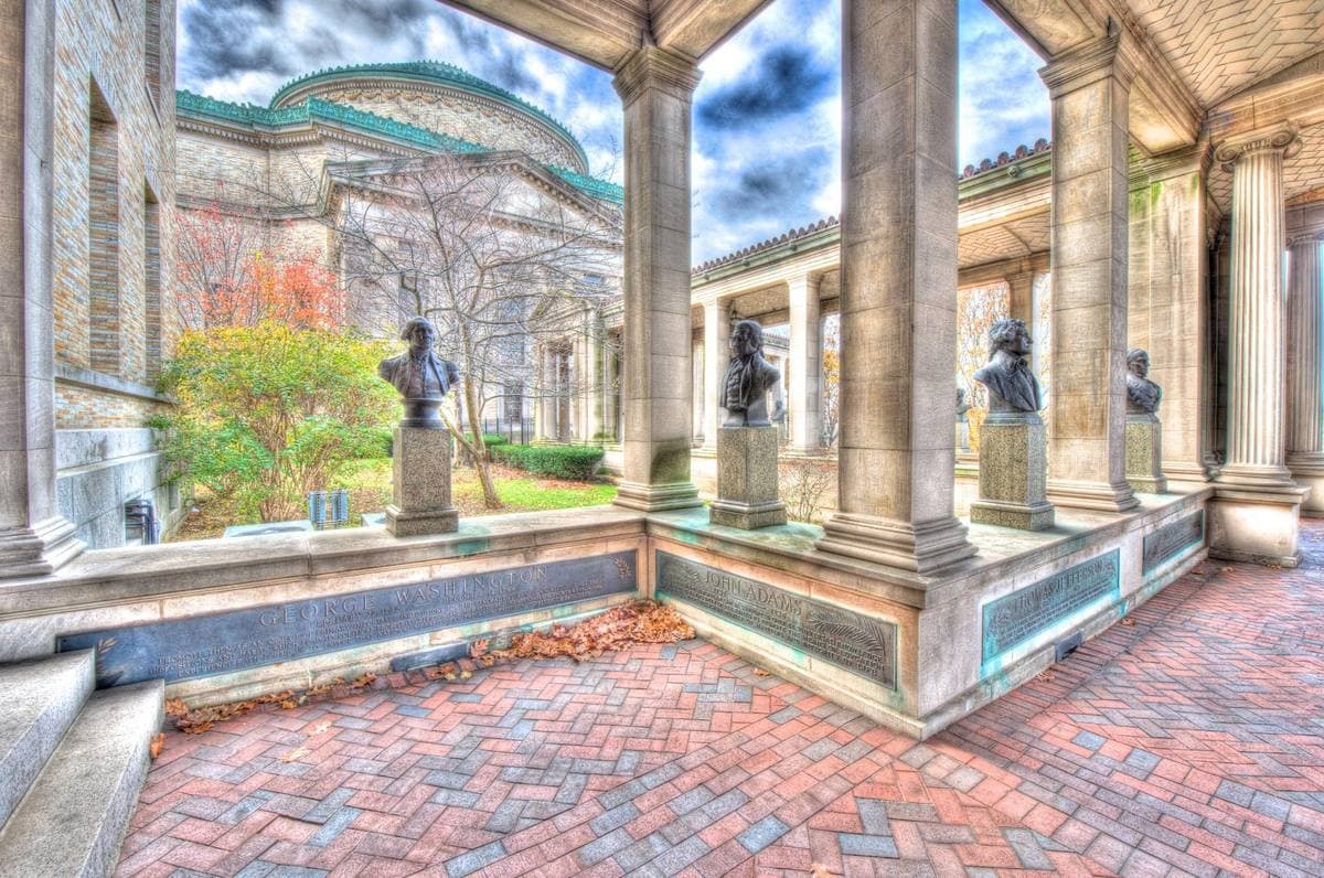 Bronze busts in a stone colonnade, with a green copper dome beyond