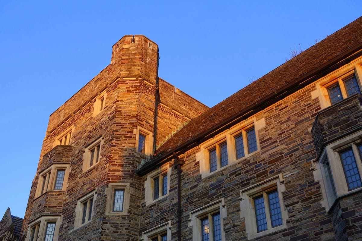 Red-brown stone tower and slate-roofed range of Holder Hall against a deep blue sky