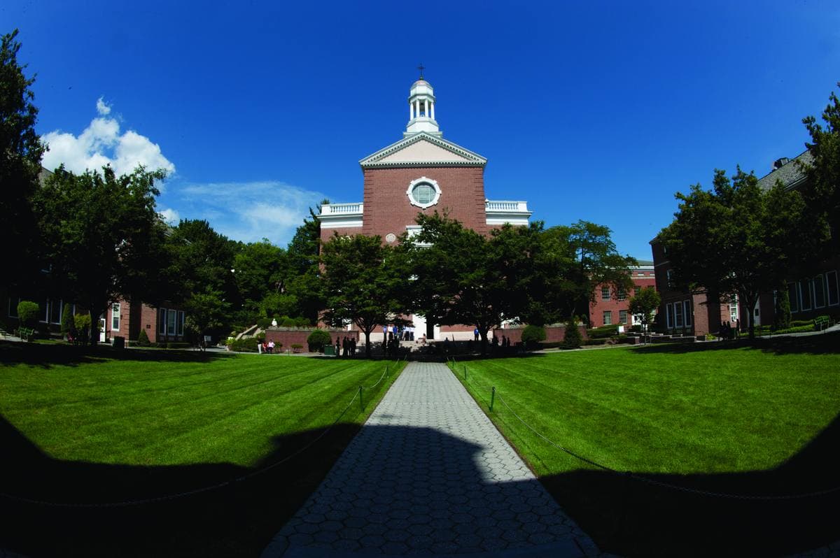 A wide green quad with a brick building and white cupola at the end of a path